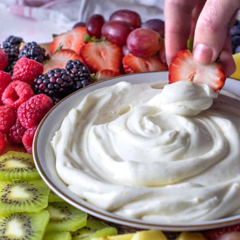 a hand swapping a strawberry through Creamy Lemon Fruit Dip