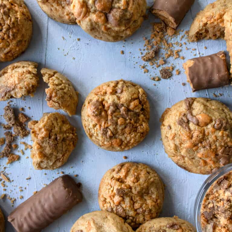 Peanut butter butter finger cookies on a blue background with some of them broken and butterfinger candy bars next to them.