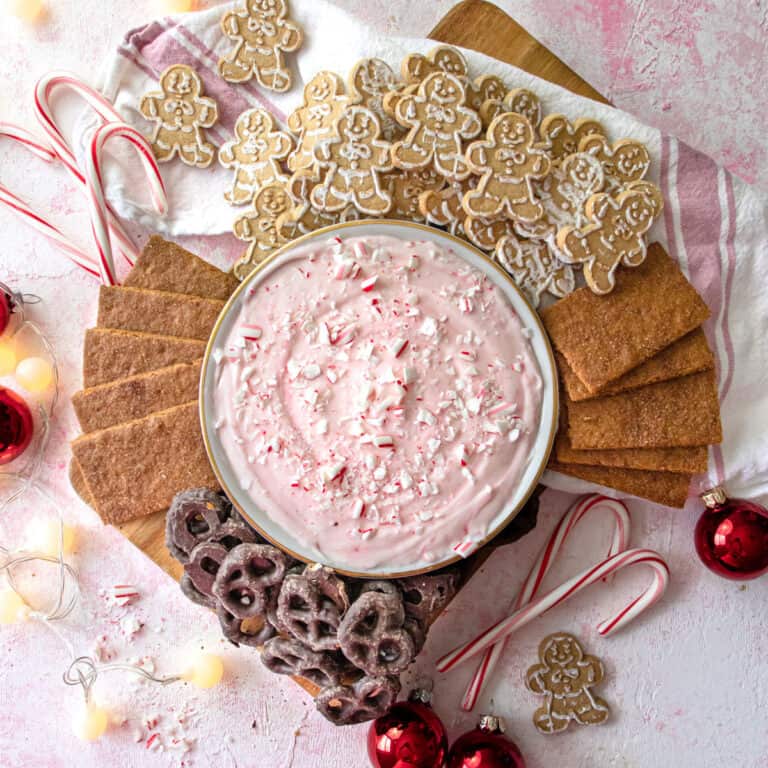Peppermint candy cane dip in a bowl with pretzels, grahman crackers, gingerbread men, and candy canes around it.