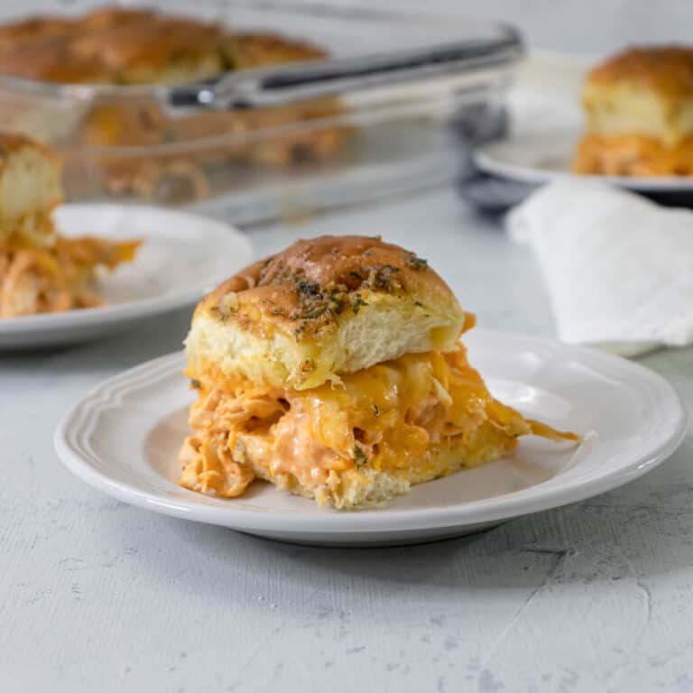 Buffalo Chicken Dip Sliders on a white plate with some in the background.