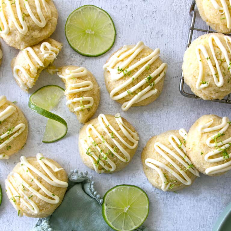 Cornmeal and lime cookies on a blue background with lime wedges next to them.