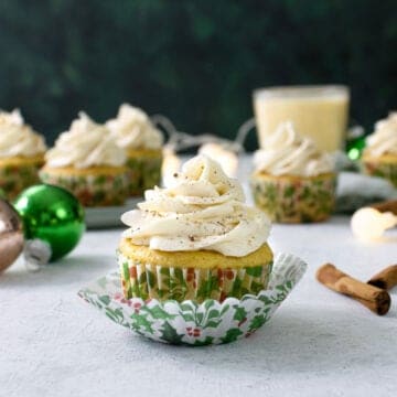Boozy Bourbon Eggnog Cupcakes on a table with christmas ornaments and egg nog in the background.