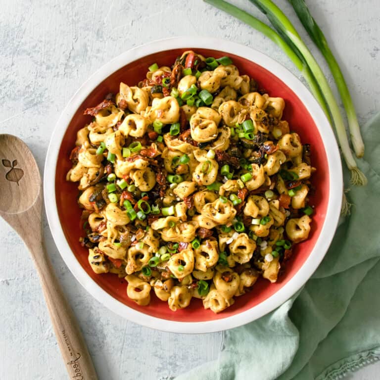 Big serving bowl of Cheese Tortellini with Sautéed Vegetables with a wooden spoon next to it.