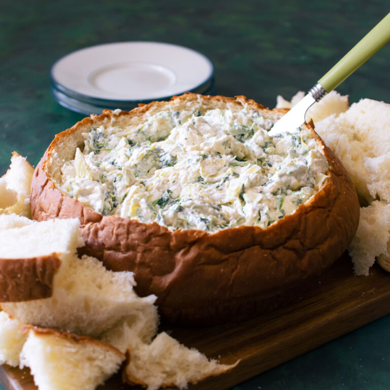 Spinach and artichoke dip in a bread bowl with a knife inside.