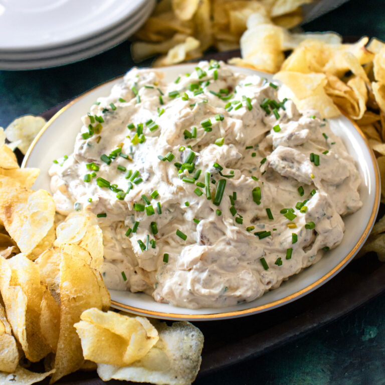 Onion and bacon dip in a bowl with chips around it.
