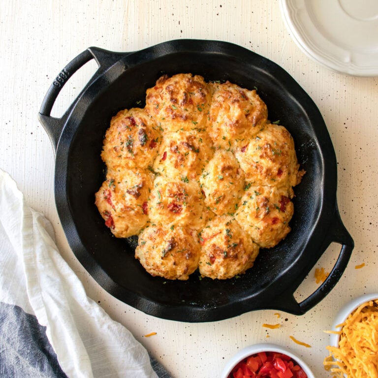 A cast iron skillet of pimento cheese biscuits with a bowl of shredded cheese and pimentos next to it.