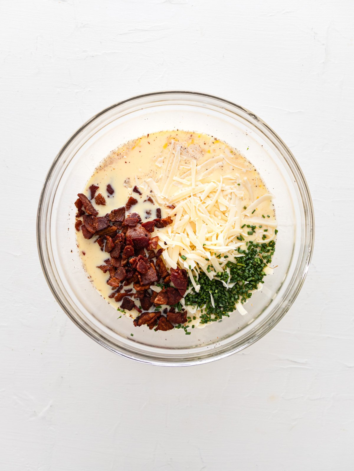 Egg mixture, bacon bits, cheese and chives in a large bowl.