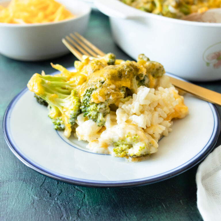 Cheesy broccoli and rice casserole scooped out onto a small white plate with a gold fork next to it.