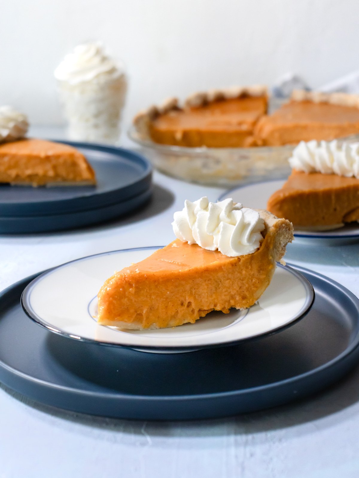 Slices of sweet potato pie with whipped cream on blue plates.