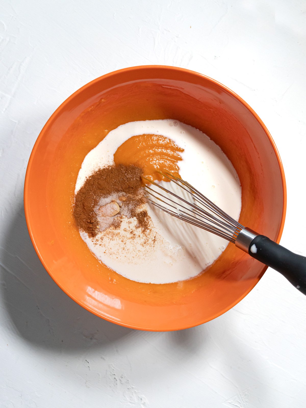 milk, spices, and sweet potato puree in a bowl with a whisk.