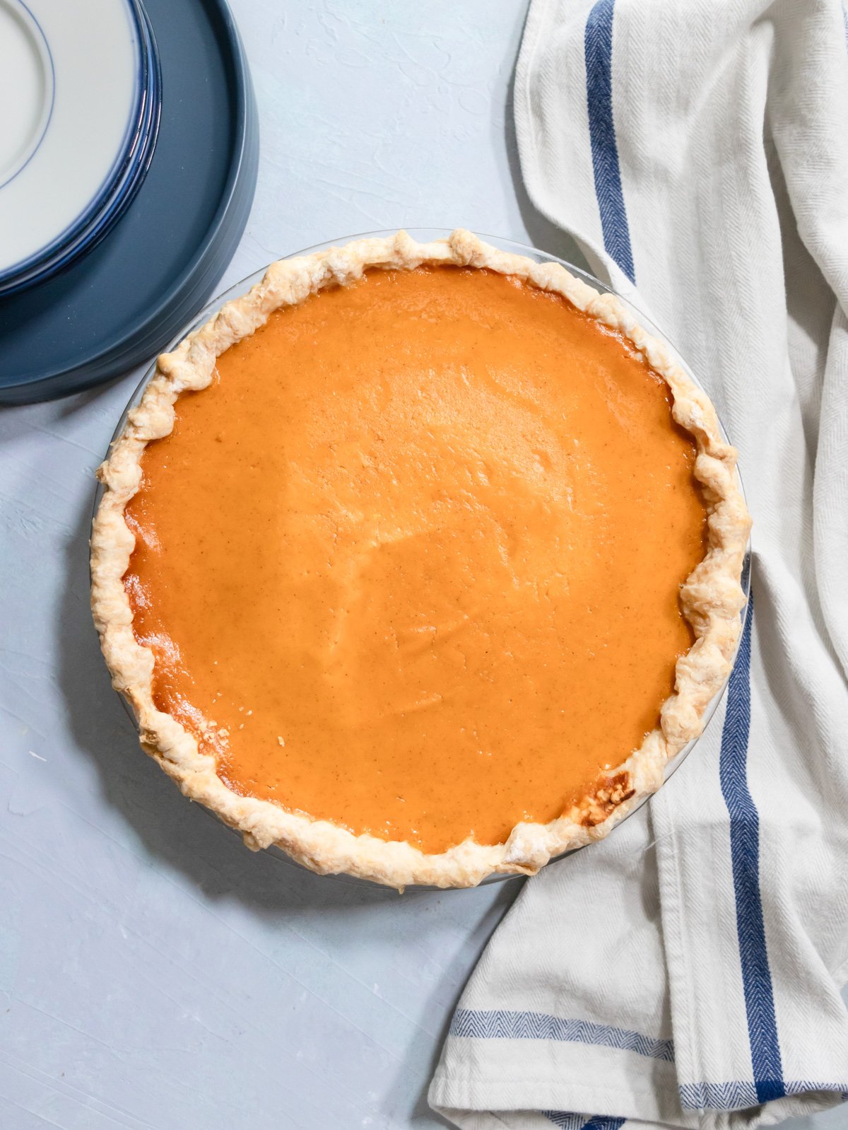 sweet potato pie baked off in a pie crust shell on a blue table with plates and a napkin around it. 