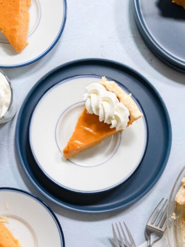 a slice of sweet potato pie on a small blue plate with whipped cream.