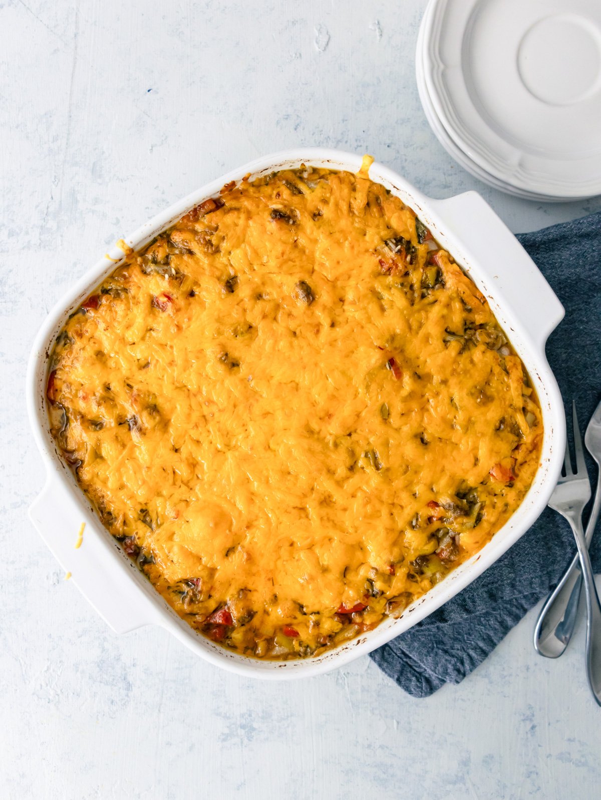 ground beef and rice casserole in a white 9x9 baking dish right after coming out of the oven with a. napkin and stack of plates next to it.
