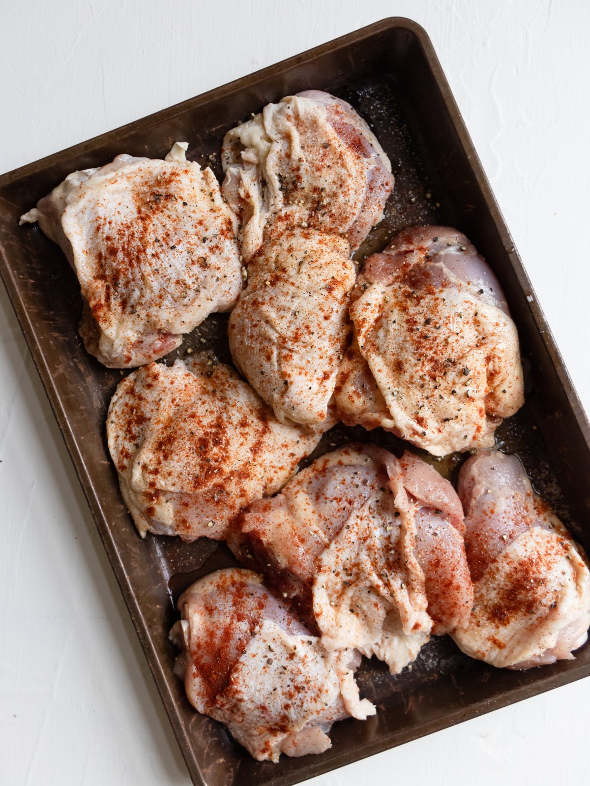 raw chicken thighs with seasoning on a baking sheet.