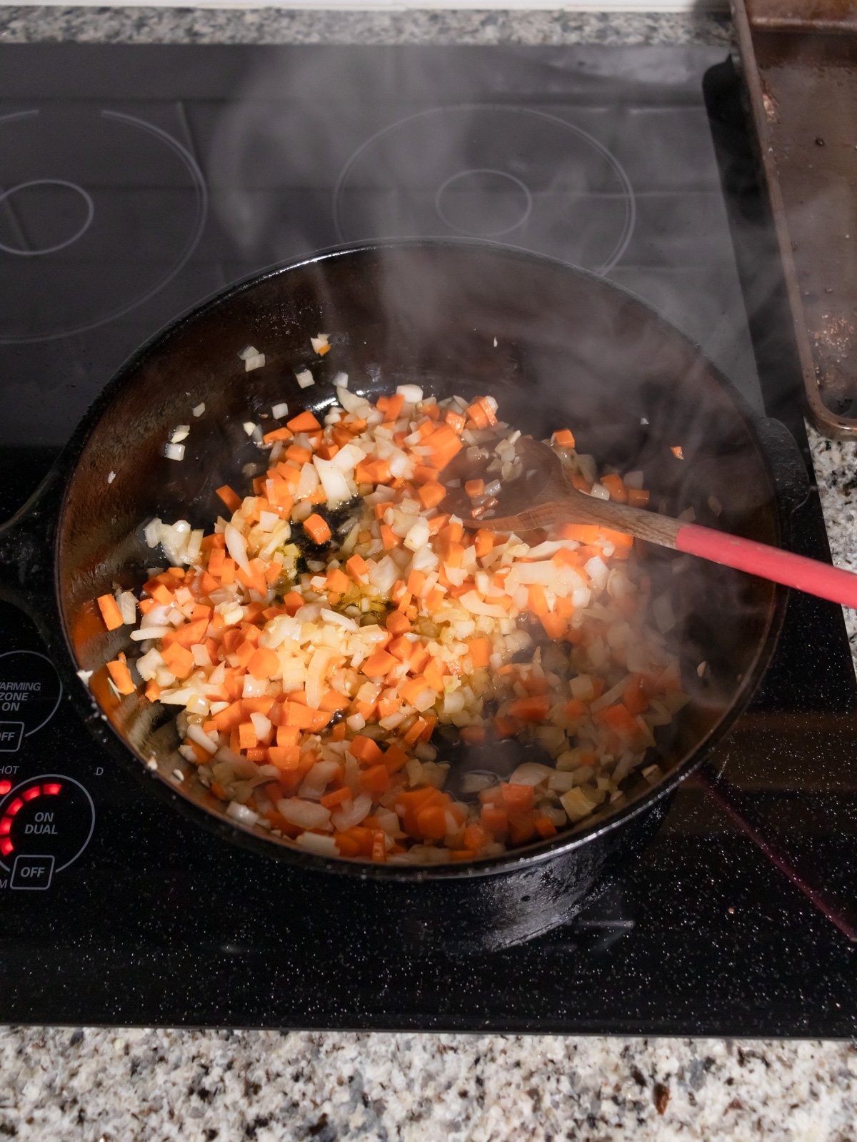 Sautéing onions garlic and carrots in a cast iron skillet on the stove.