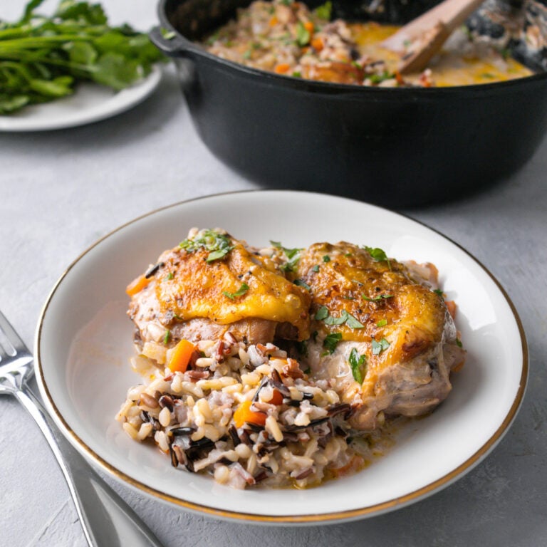 chicken thighs and rice in a white shallow bowl with a cast iron skillet in the background.