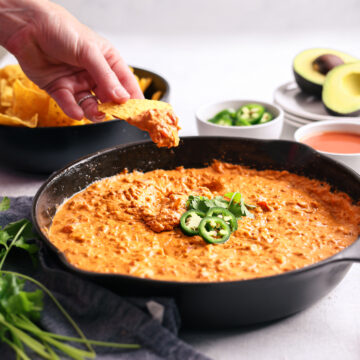 a hand scooping our a cheese dip inside a cast iron skillet with a chip.