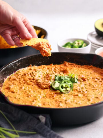 a hand scooping our a cheese dip inside a cast iron skillet with a chip.