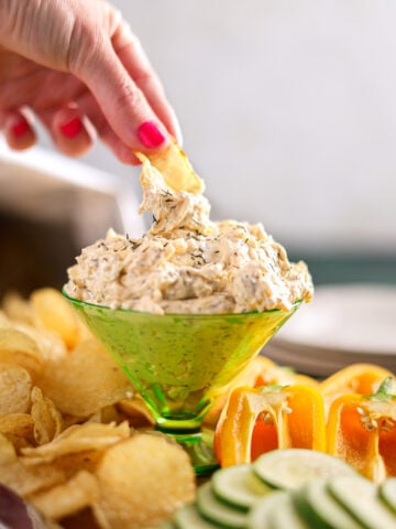 a hand dipping a chip into a cucumber cream cheese dip.