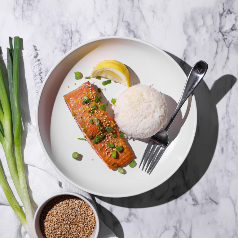 salmon, rice and a lemon on a plate with green onions and sesame seeds next to it