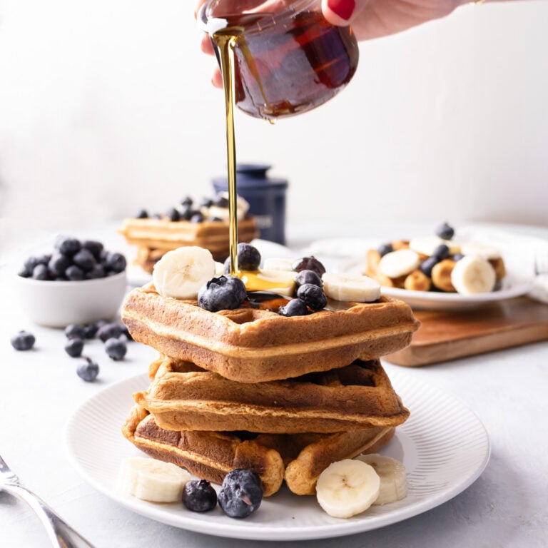 pouring maple syrup on top of a stack of waffles.