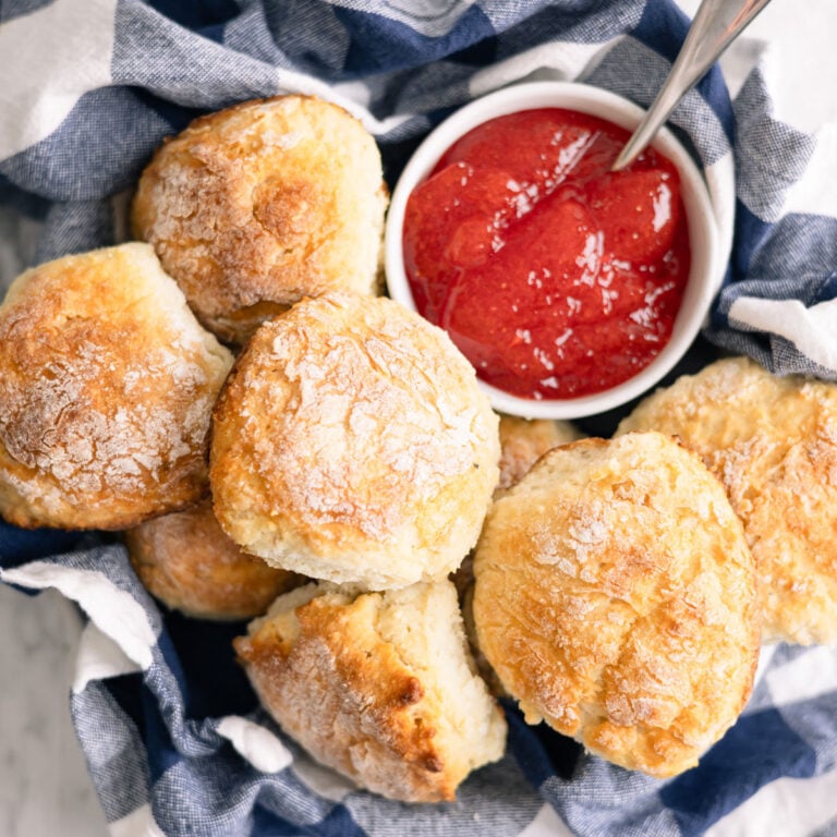 mashed potato biscuits in a basket with jelly next to them.