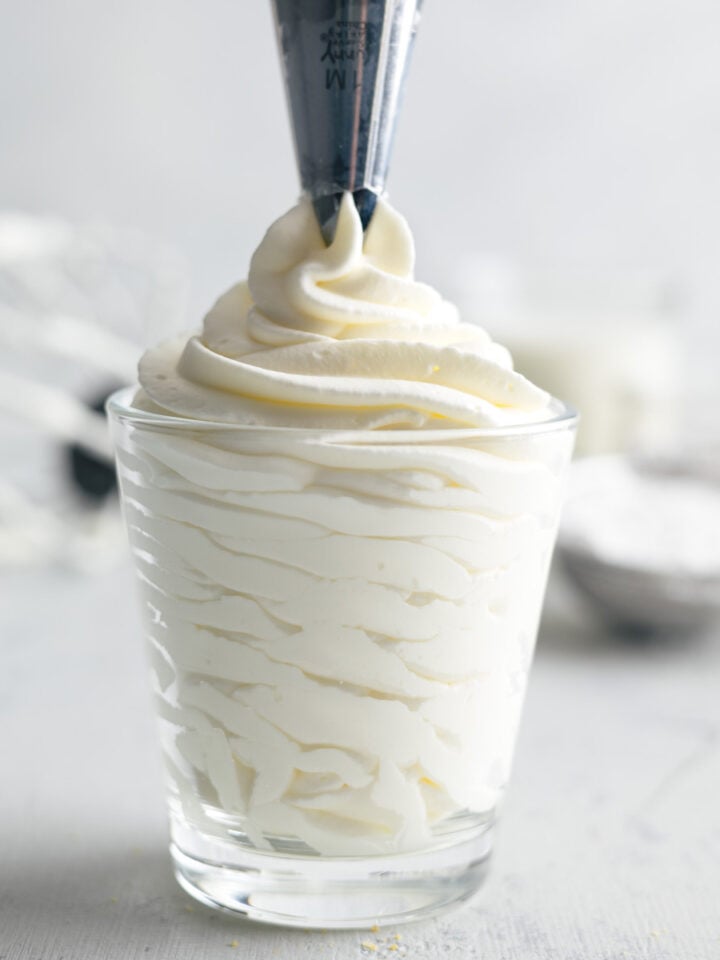 pipping homemade whipped cream into a clear cup with a piping bag nd tip.