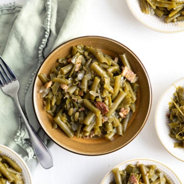 green beans in a brown bowl with little bowls and a green napkin around it.