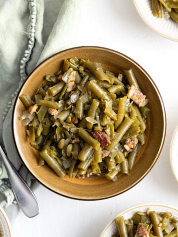 green beans in a brown bowl with little bowls and a green napkin around it.