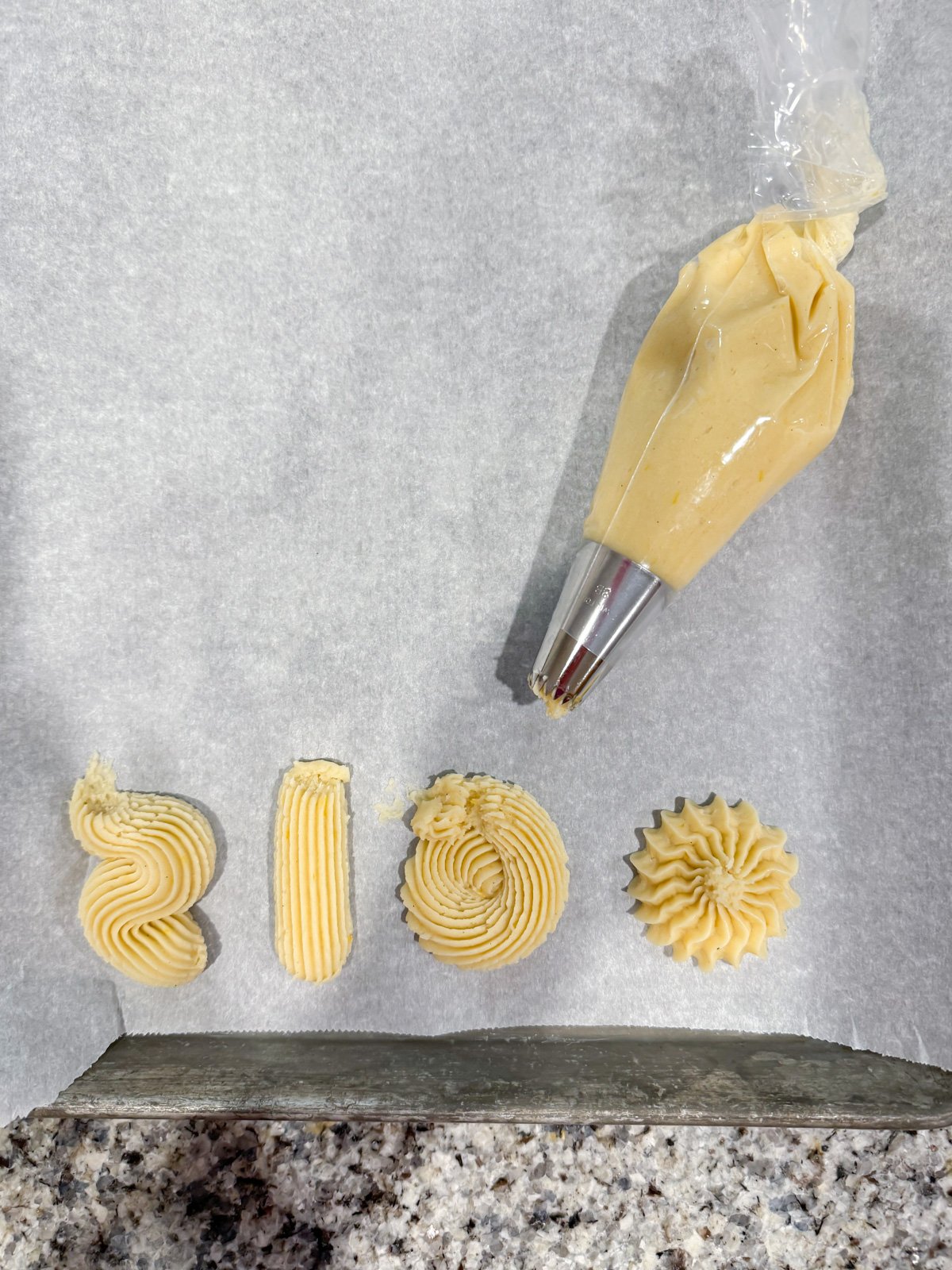 piping out butter cookie shapes on a baking sheet.