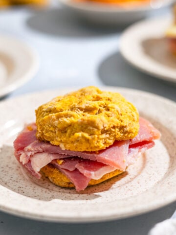 small plate with a sweet potato biscuit stuffed with country ham in it.