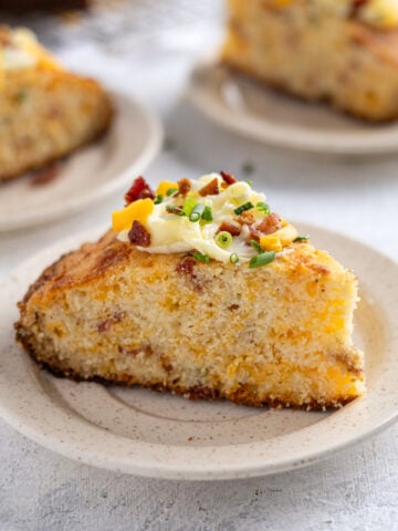 A slice of bacon and cheddar cornbread on a plate with butter on top.