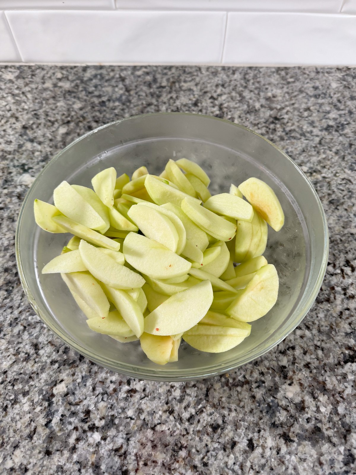 A clear bowl of sliced green apples.