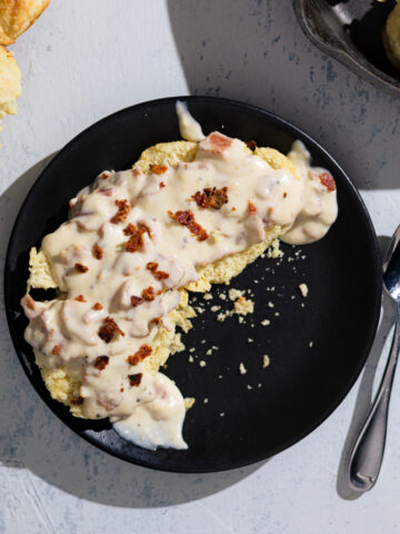 Biscuits on a plate with bacon gravy spooned over and a spoon next to it.