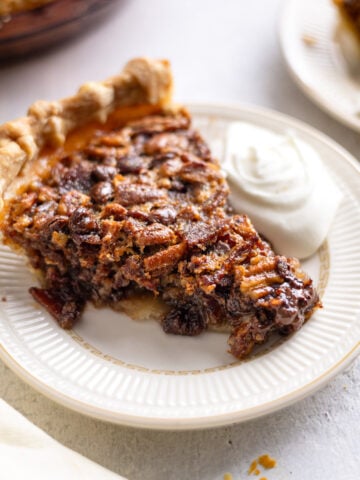 A slice of bourbon bacon pecan pie on a white plate with a scoop of whipped cream on top.