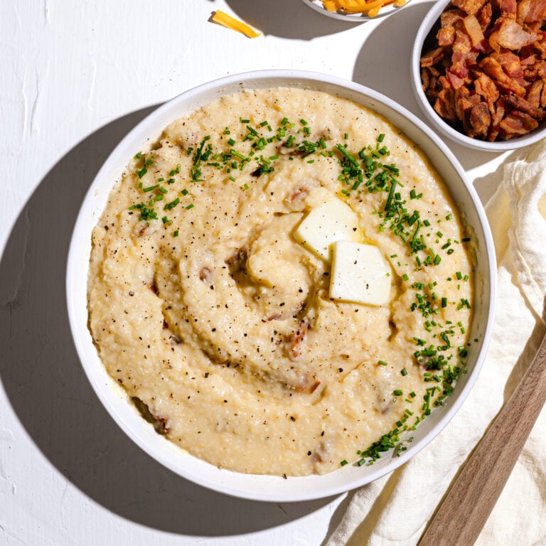 bacon cheddar grits in a large serving bowl with a wooden spoon and bacon bits next to it