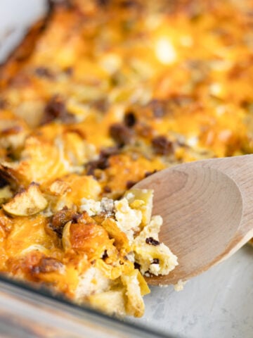 A wooden spoon scooping out a breakfast casserole from a baking dish.