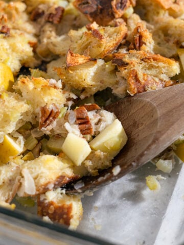 sourdough dressing with apples and pecans being scooped out by a wooden spoon.