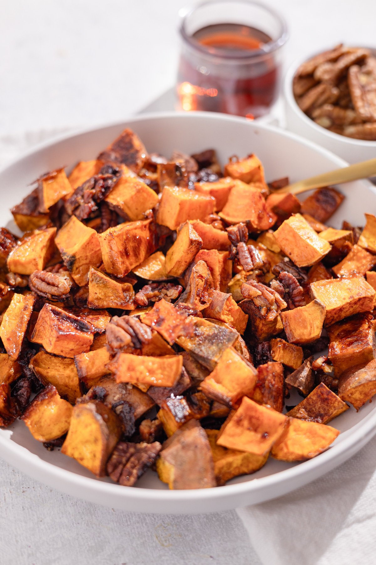 roasted sweet potatoes and pecans in a big serving bowl with a gold spoon.