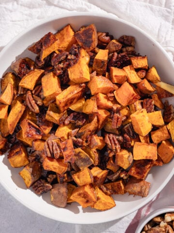 bowl of roasted sweet potatoes and pecans on a pink background