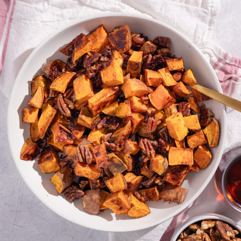 bowl of roasted sweet potatoes and pecans on a pink background