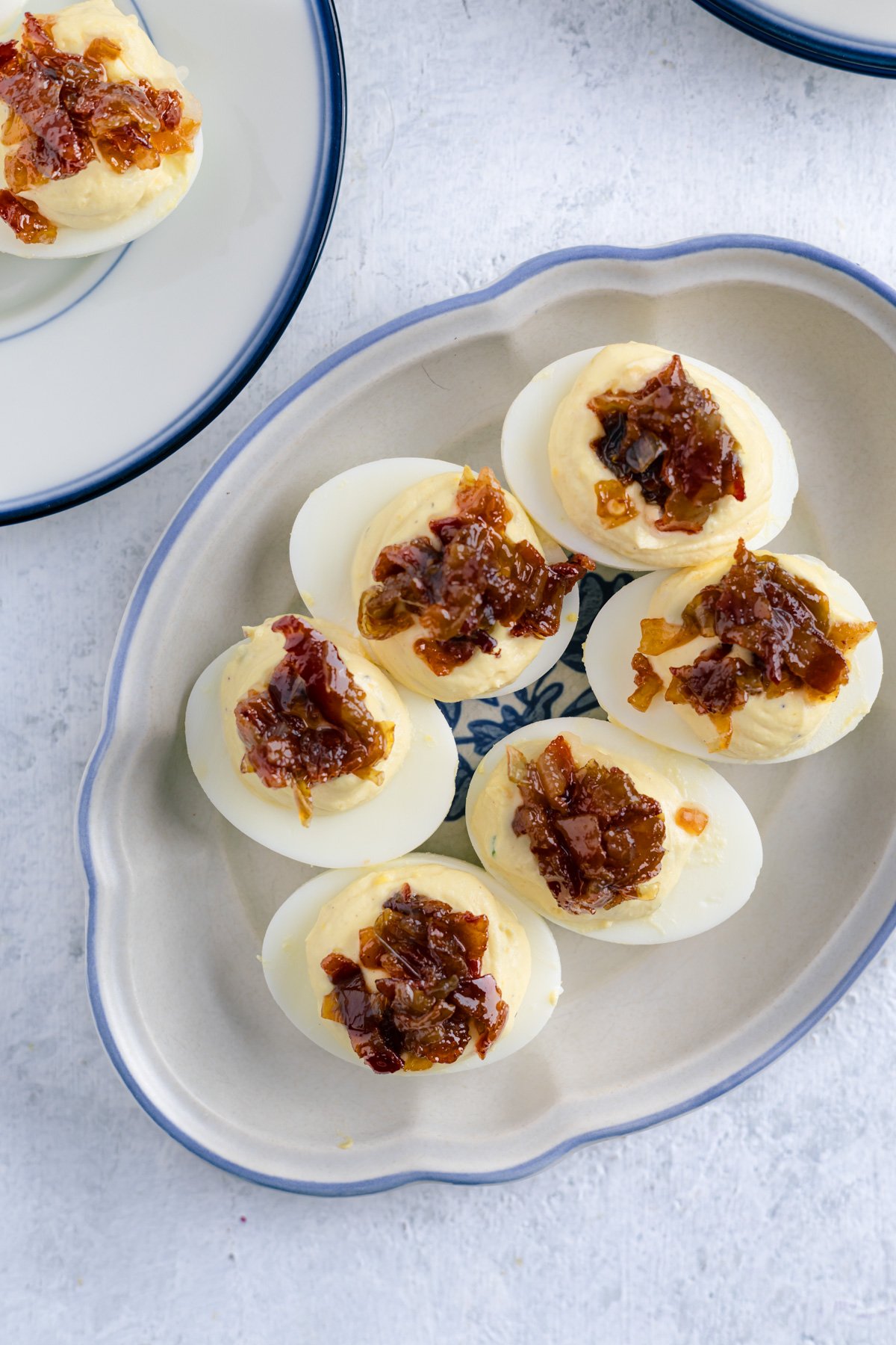 deviled eggs topped with bacon jam on a small blue platter