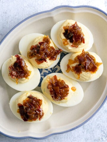 deviled eggs with bacon jam on top n a small platter.