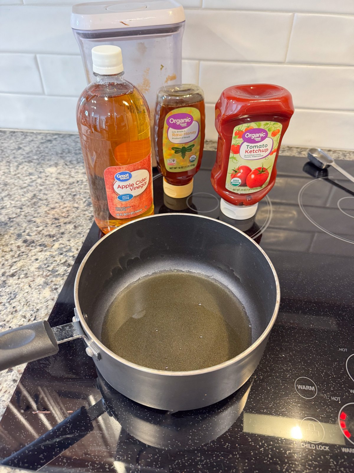 A pot in the stove with bottles of vinegar, ketchup, and honey on top of the stove. 