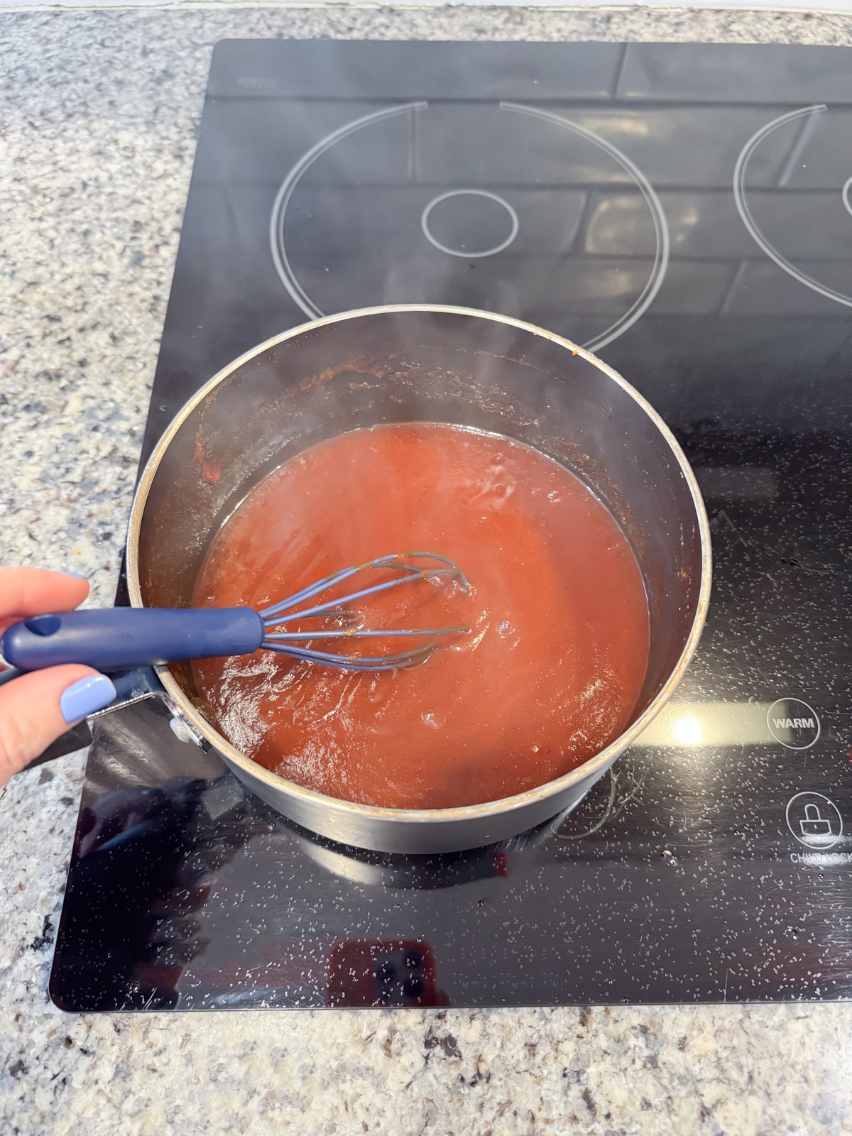 Whisking together bbq sauce that is cooking on the stove.