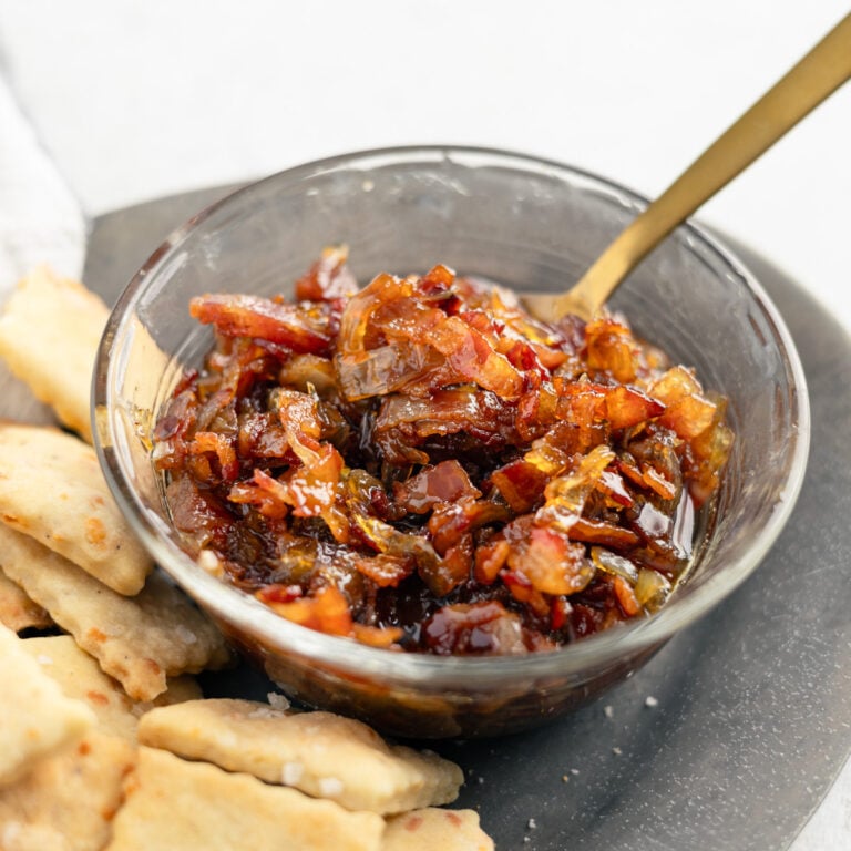 bacon jam in a bowl with crackers around it and a spoon inside.