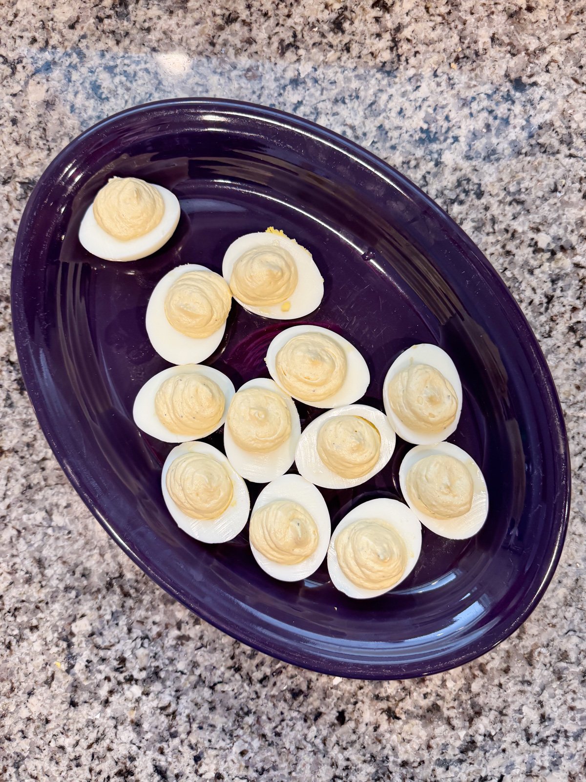 deviled eggs that have just been filled with the yolk filling on a purple platter.
