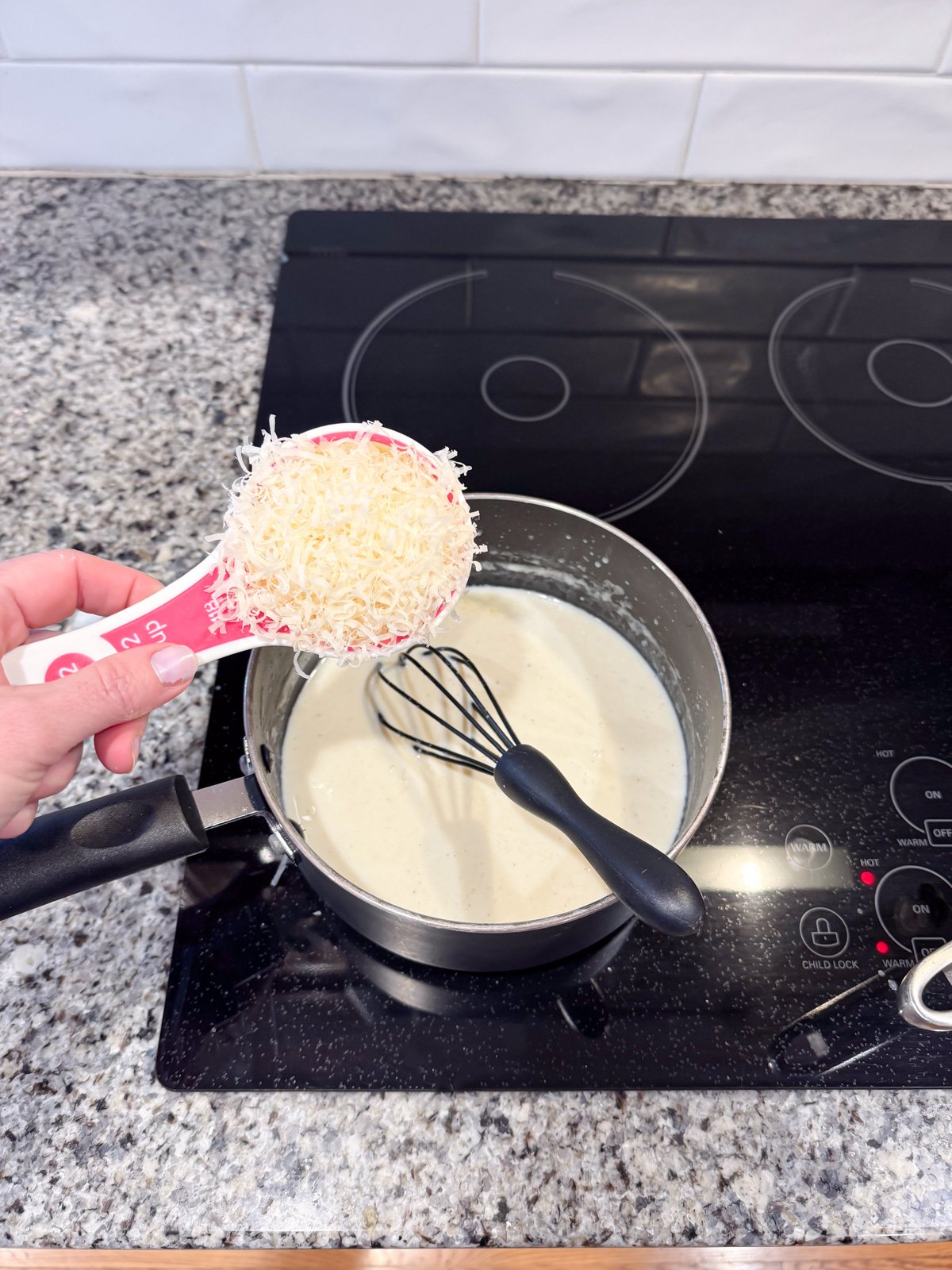 Adding parmesan cheese to a white sauce roux mixture in a saucepan. 