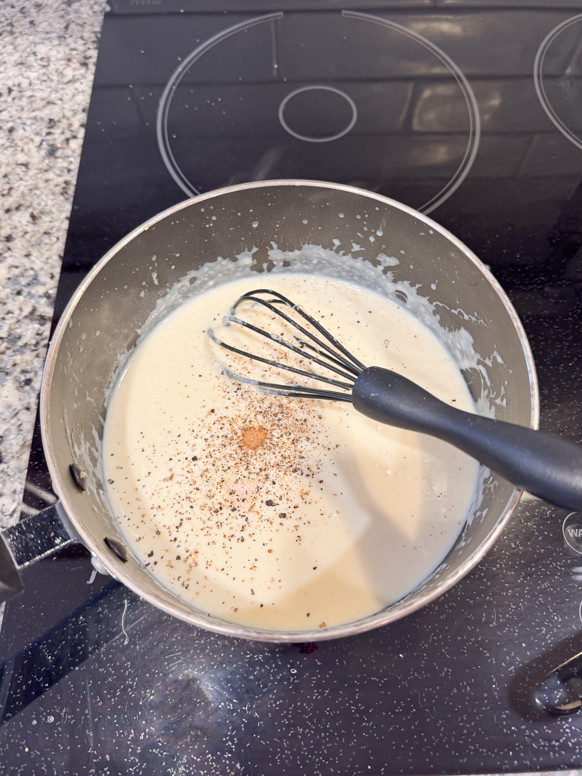 Whisking in salt and pepper to a roux mixture on the stove. 