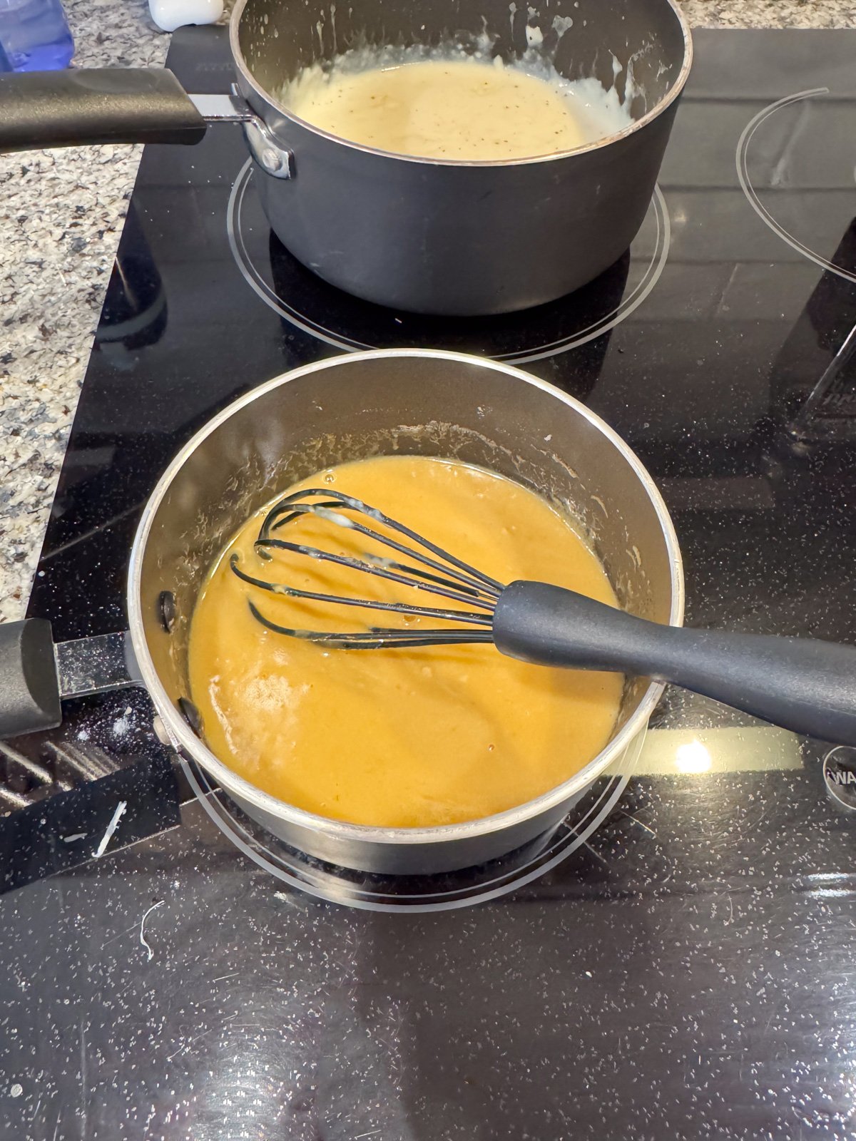 Whisking together a butter and mustard sauce on the stove in a saucepan.